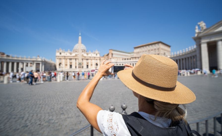 Woman in hat capturing Vatican in early morning light.