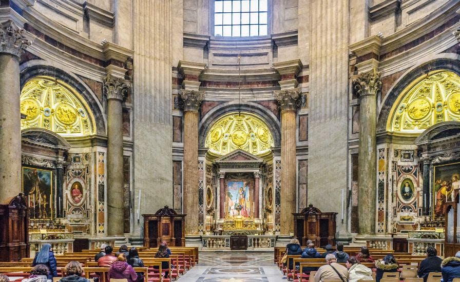 St. Peter's Basilica interior with seated congregation, showcasing famous artworks.