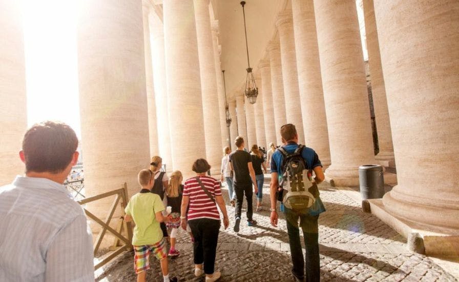 A group of people walking down a walkway with pillars