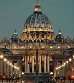 The illuminated dome of the Vatican's Basilica, an iconic symbol, shines brightly against the night sky.