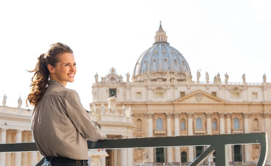 A woman on a balcony gazes at the Vatican, with St. Peter's Basilica in the background.