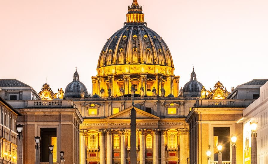 The Vatican City illuminated at dusk, with the Basilica shining brightly beneath it.