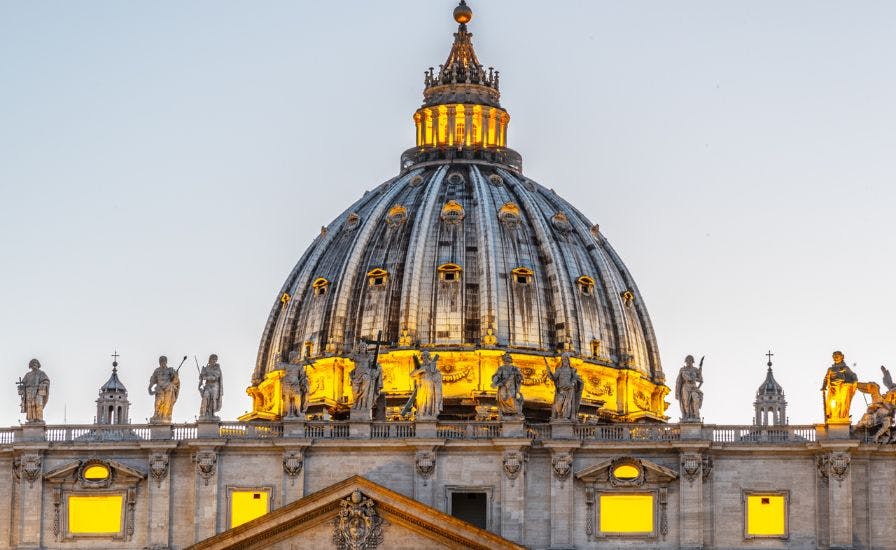 The illuminated dome of the Vatican at dusk, showcasing its architectural beauty. Experience it with the Dome Tour.
