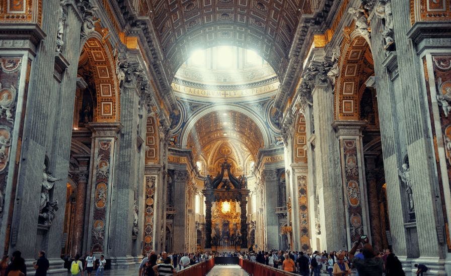 Inside a cathedral, people walk around and the Chair of St. Peter from St. Peter's Basilica.
